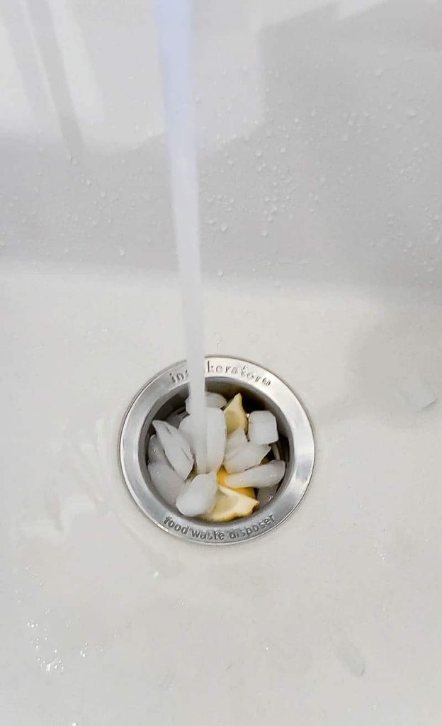 A steady stream of water pours into a garbage disposal drain that's filled with ice cubes and lemon wedges.