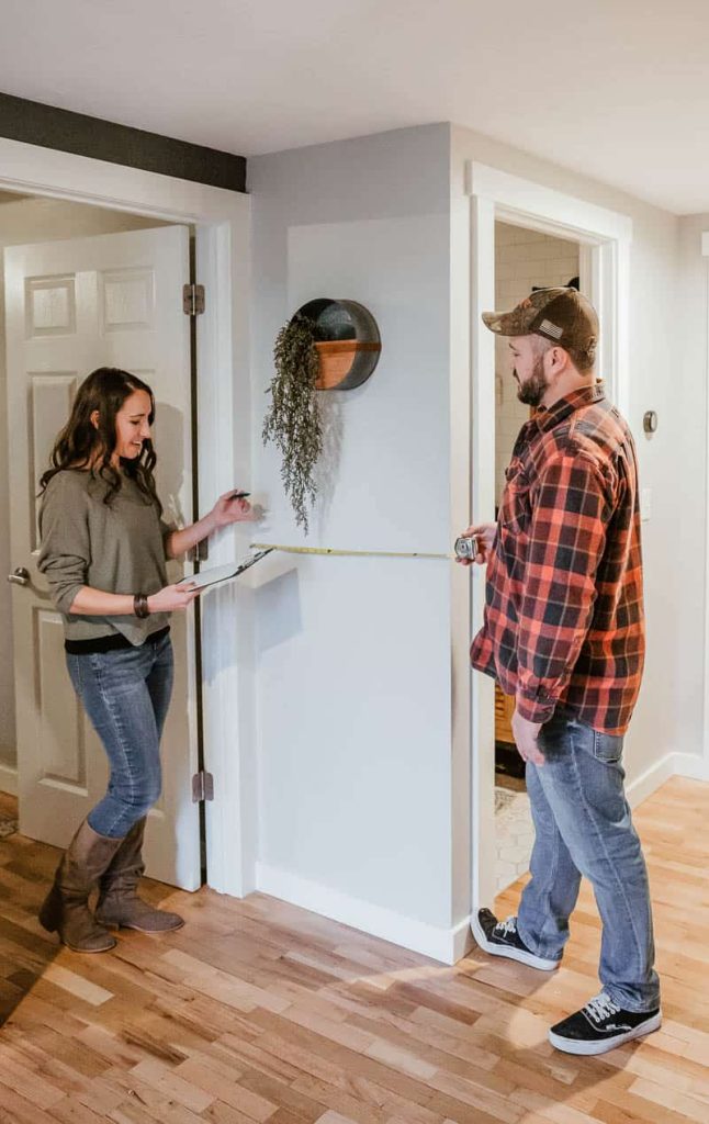 Husband and wife measuring wall with tape measure to create a plan for renovating