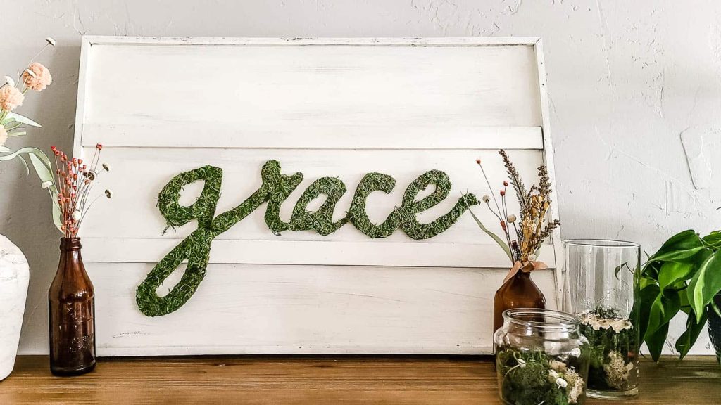 A wooden serving platter with the word "grace" written across the center with preserved moss.