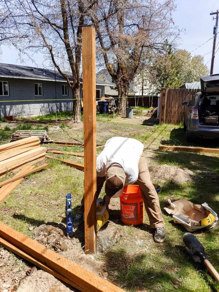 shows a man leveling out the fence post in the cement