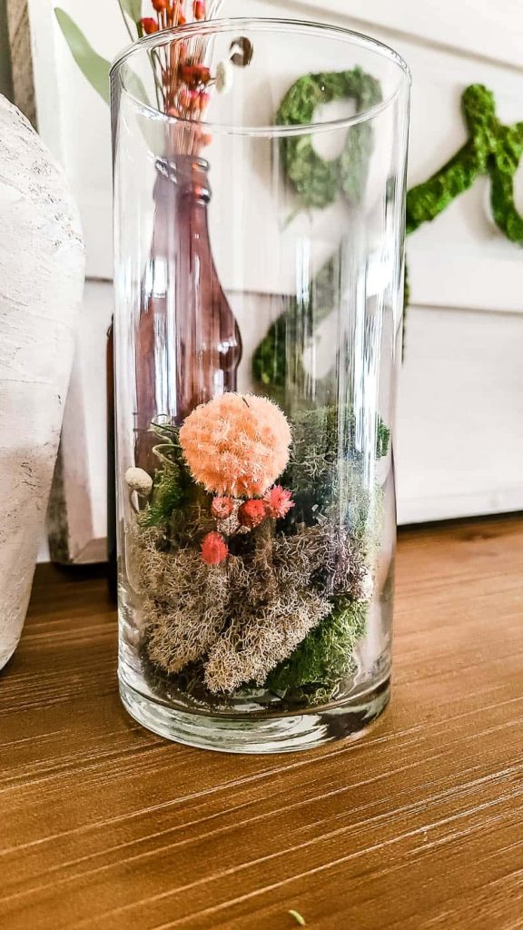A close up image of a glass vase filled with rocks, faux moss and flowers with Spring colors.
