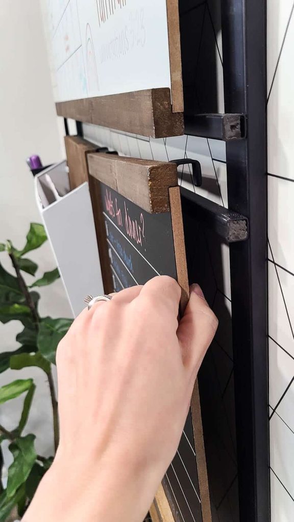 An image of a woman setting up the family command center by hanging the chalkboard memo sign on the black metal frame.