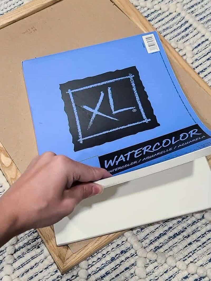 hand holding edges of watercolor paper pad showing the inside pages for DIY boho wall decor