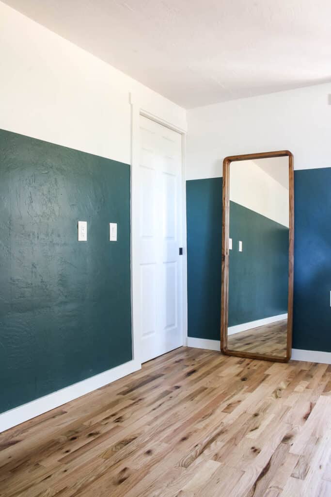 Newly painted master bedroom wall with green on bottom and white on top of walls with large rectangular mirror leaning on it beside the white walk in closet pocket door