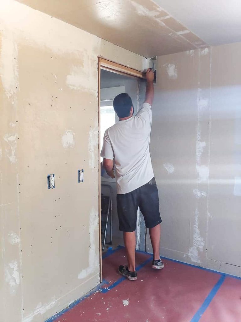 man applying trowel texture at the top of the wall and ceiling beside the walk in closet pocket door showing where the drywall needed to be patched and repaired where a reach in closet was removed