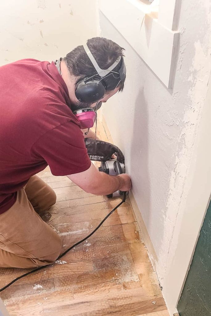 Man sanding hardwood floors with belt sander in closet 