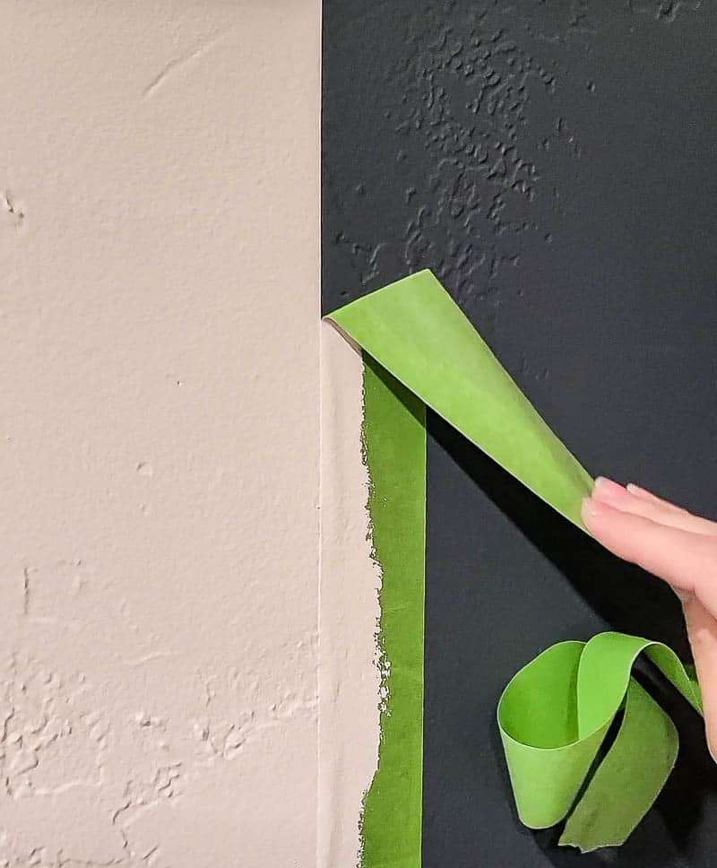 hand of a woman peeling off the green painter's tape with nice crisp paint edge from the wall between the white and gray painted wall