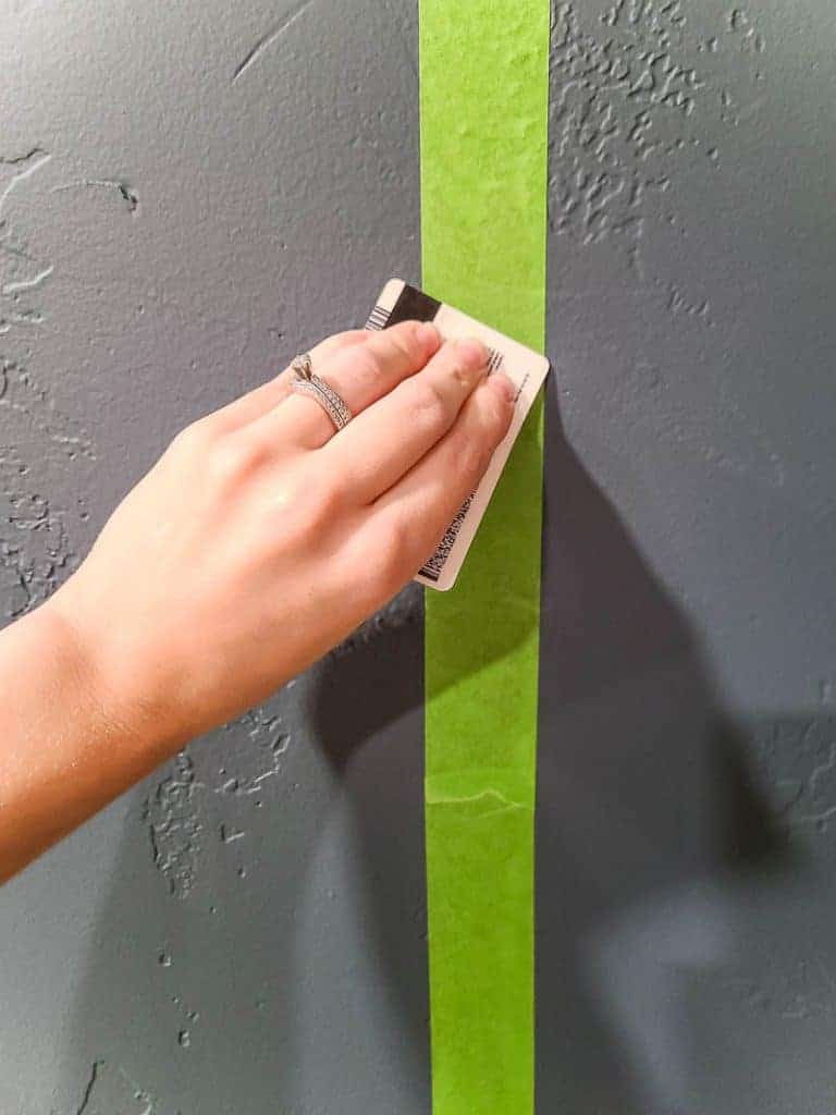 Hand of a woman with a ring holding a card swiping over the green painter's tape on the gray wall