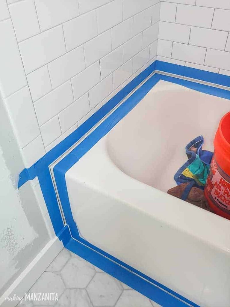 Painter's tape all over the edges of the bathtub before getting caulked and white subway bathroom tiles up to the bathroom floor