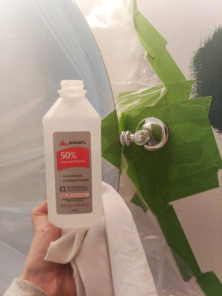 Woman holding bottle of rubbing alcohol and white cloth and bathroom fixture covered in plastic and taped off at the back