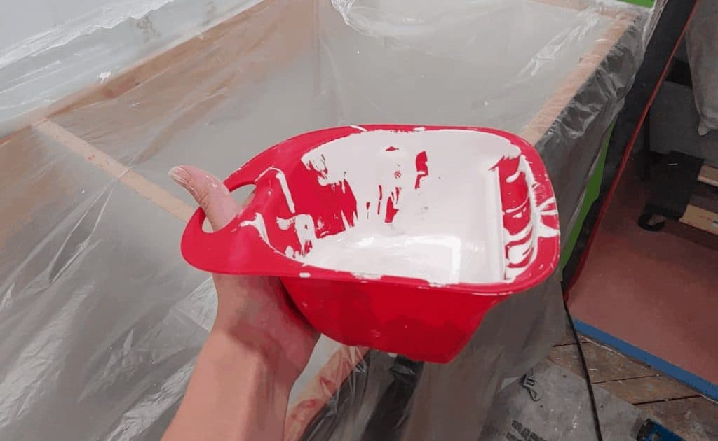 Hand holding The Handy Craft Cup small red cup filled with white paint which makes is easy to hold in your hand and move around the room as you cut in paint