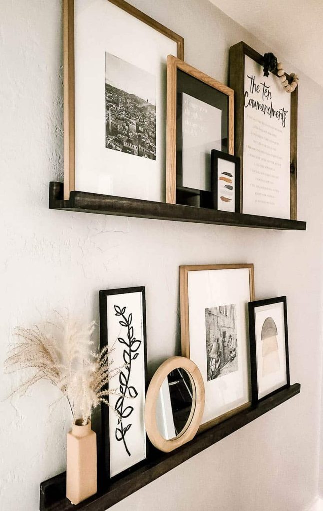 Picture ledge shelving a hallway styled with monochromatic wall decor leaning against the wall 