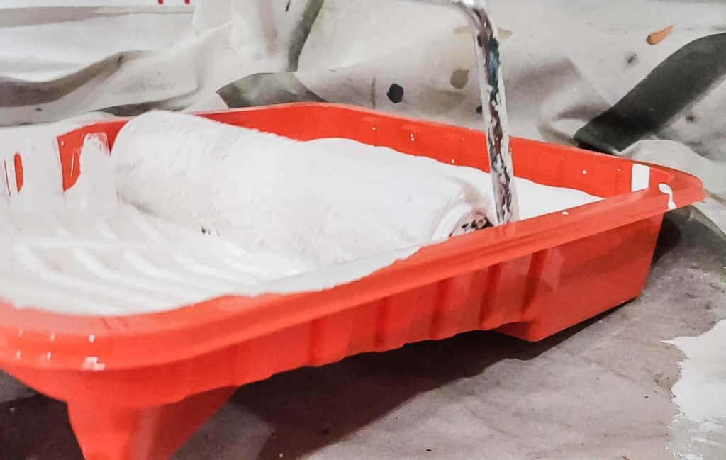Paint roller dipped into the paint tray with white paint