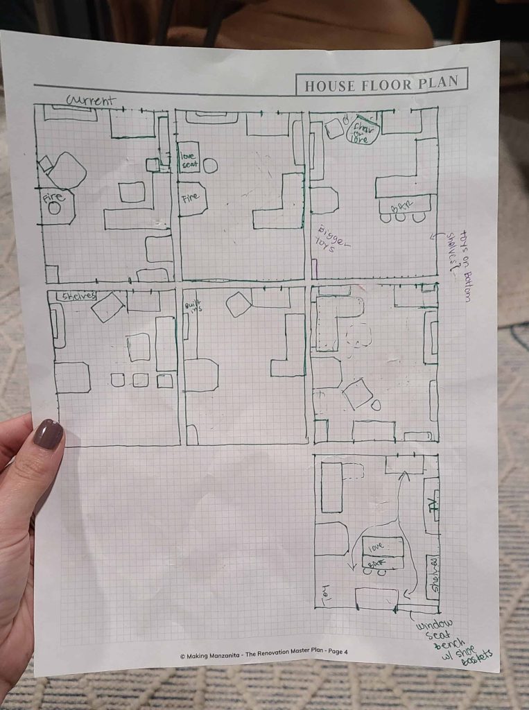 A woman holds a sheet of grid paper with seven different hand-drawn rectangular living room layout plans. The sheet features handwritten notes with arrows indicating where certain things would be stored.