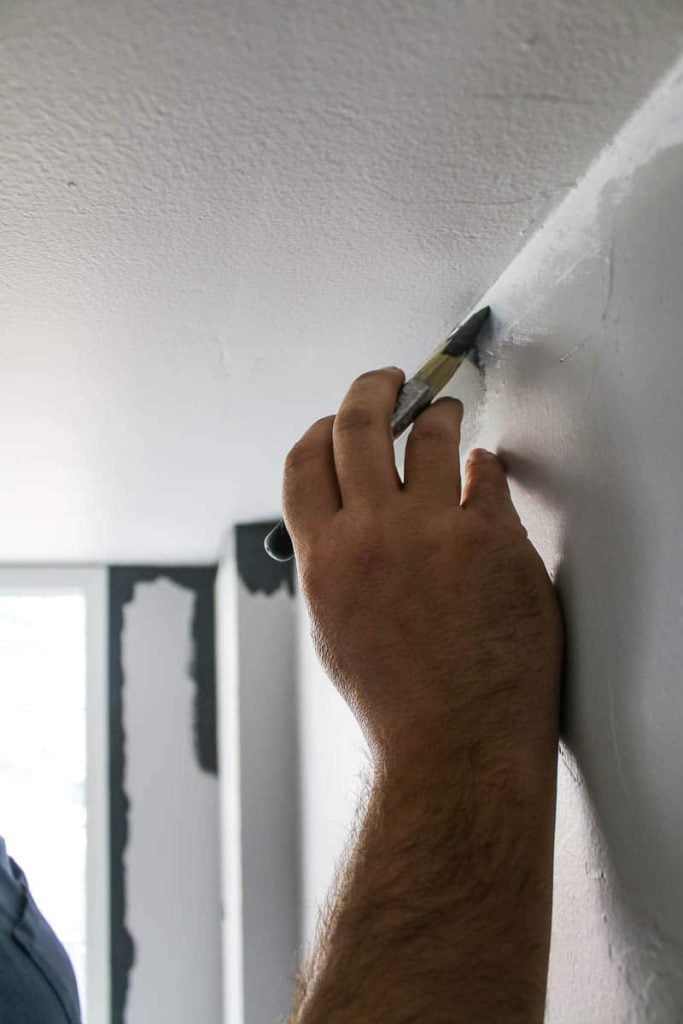 Hand holding an angeled paint brush with a steady hand cutting in paint on the wall with gray paint where the wall pieces the ceiling corner