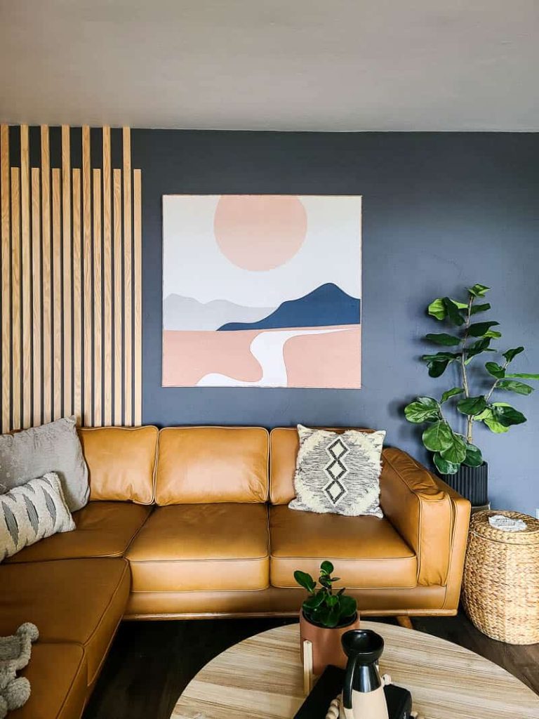 Full view of fabric wall art using society6 tapestry with mountains and sunset in the modern boho living room hanging on the wall beside wood accent wall above the article leather sectional and boho throw pillows