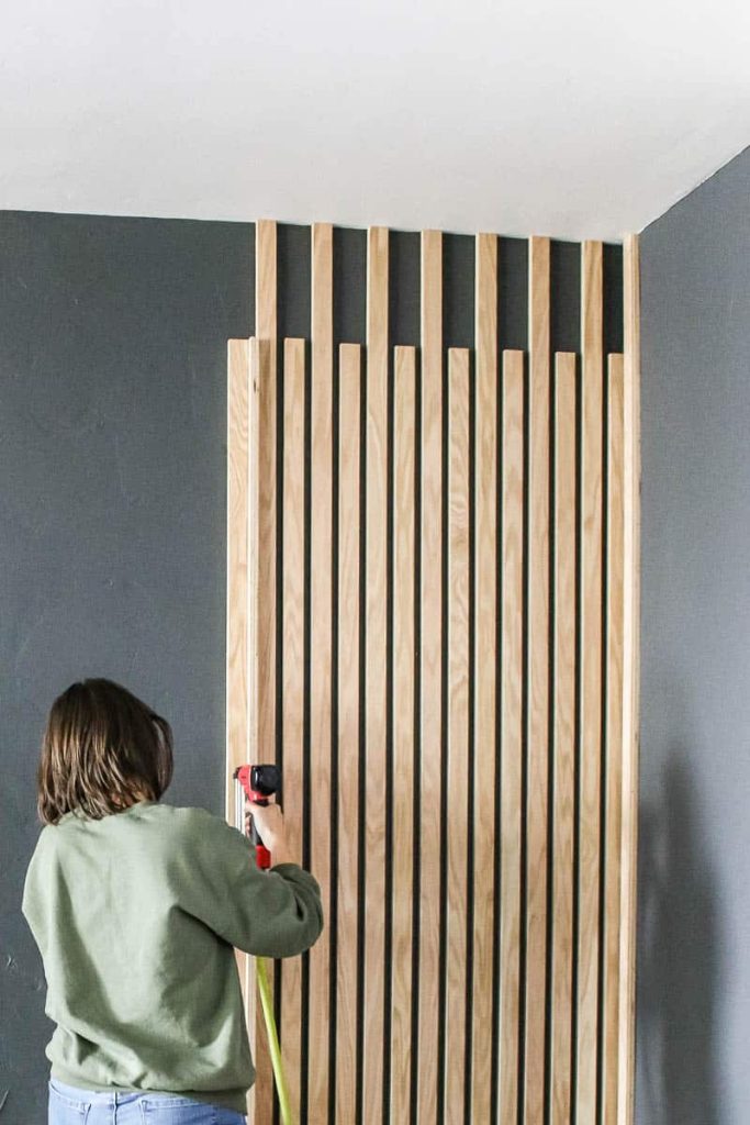 Front view of the wood slats attached to the wall and woman attaching vertical wood slats using a brad nailer