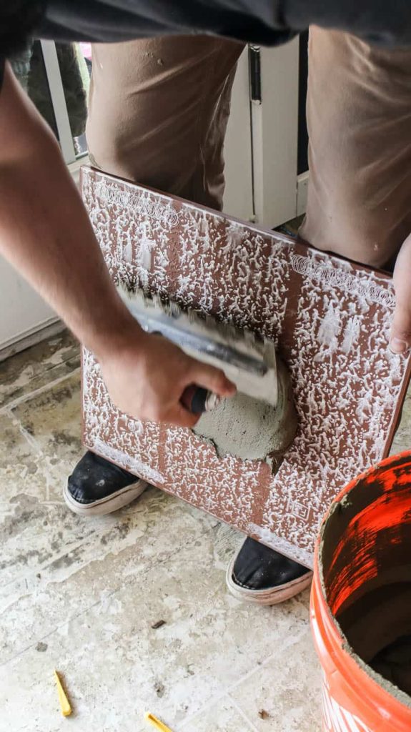 Man applying mortar at the back of the tile with the back butter technique
