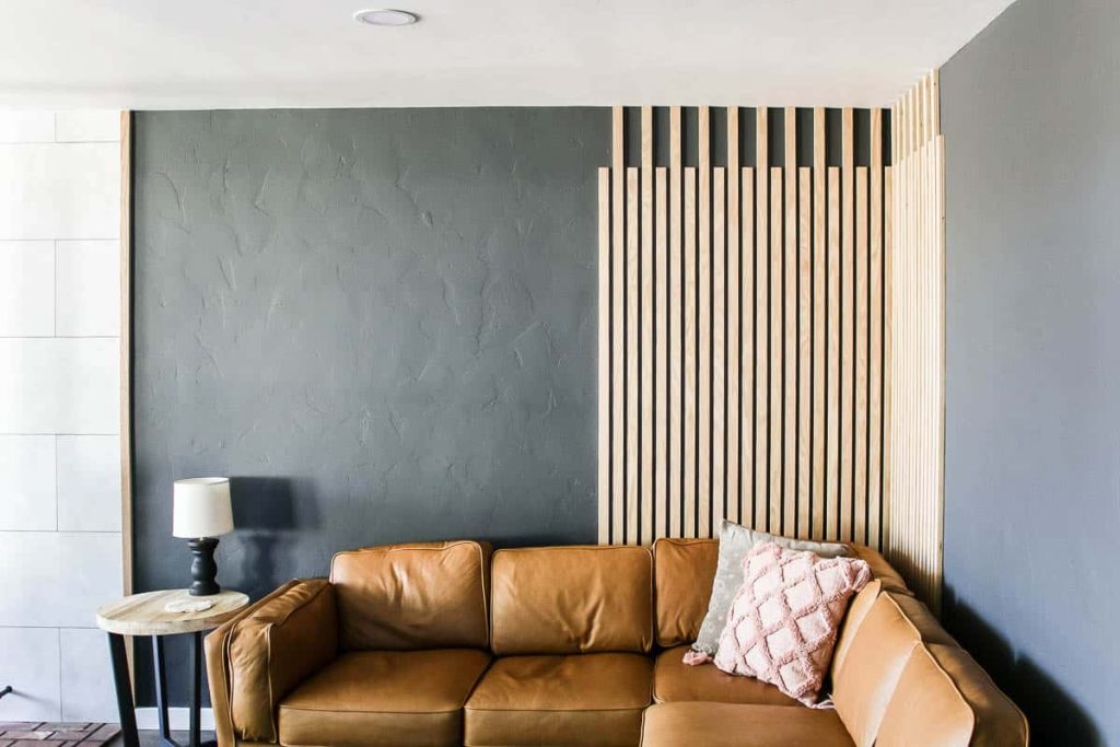 DIY Slat Wall as Wood Accent Wall in the living room with wood side table, lamp, leather couch and throw pillows