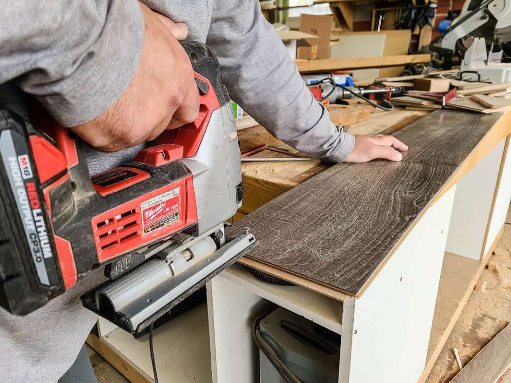 Man cutting the laminate on workbench using jigsaw for the last row