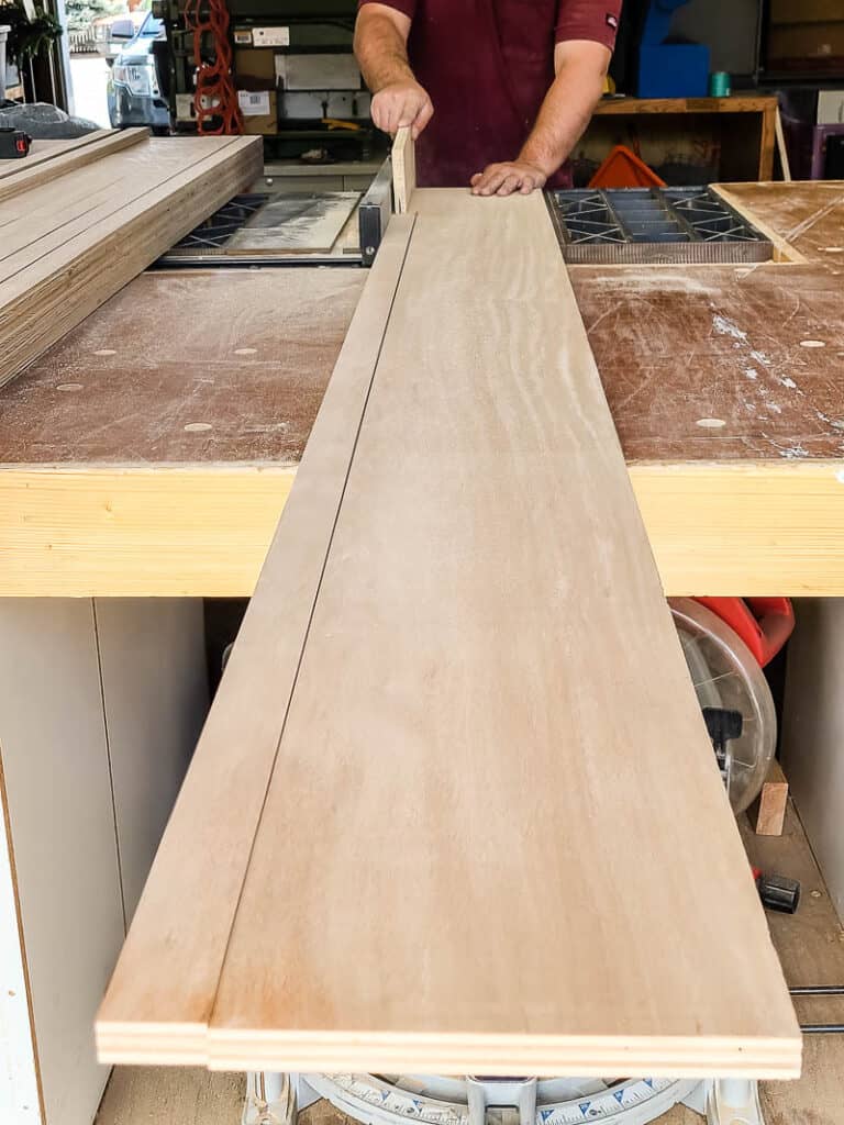 Man cutting plywood sheet down into wood slats with a table saw for accent wall