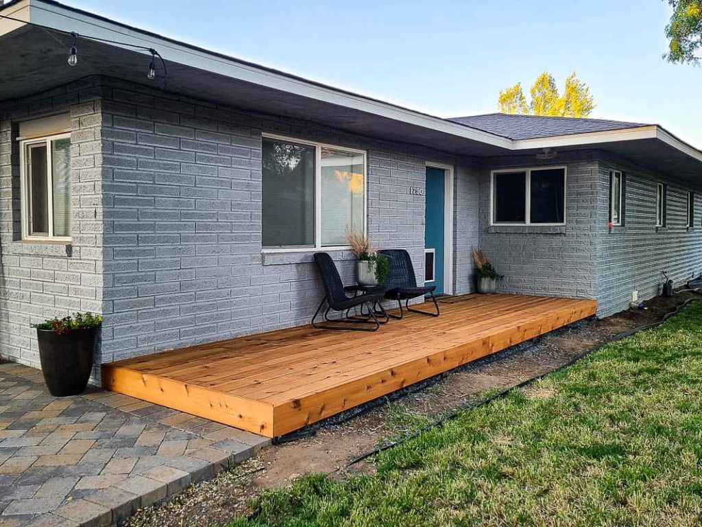 Full view of the backyard with wood deck board with two black chairs and center table with plants under the window and back door after the makeover