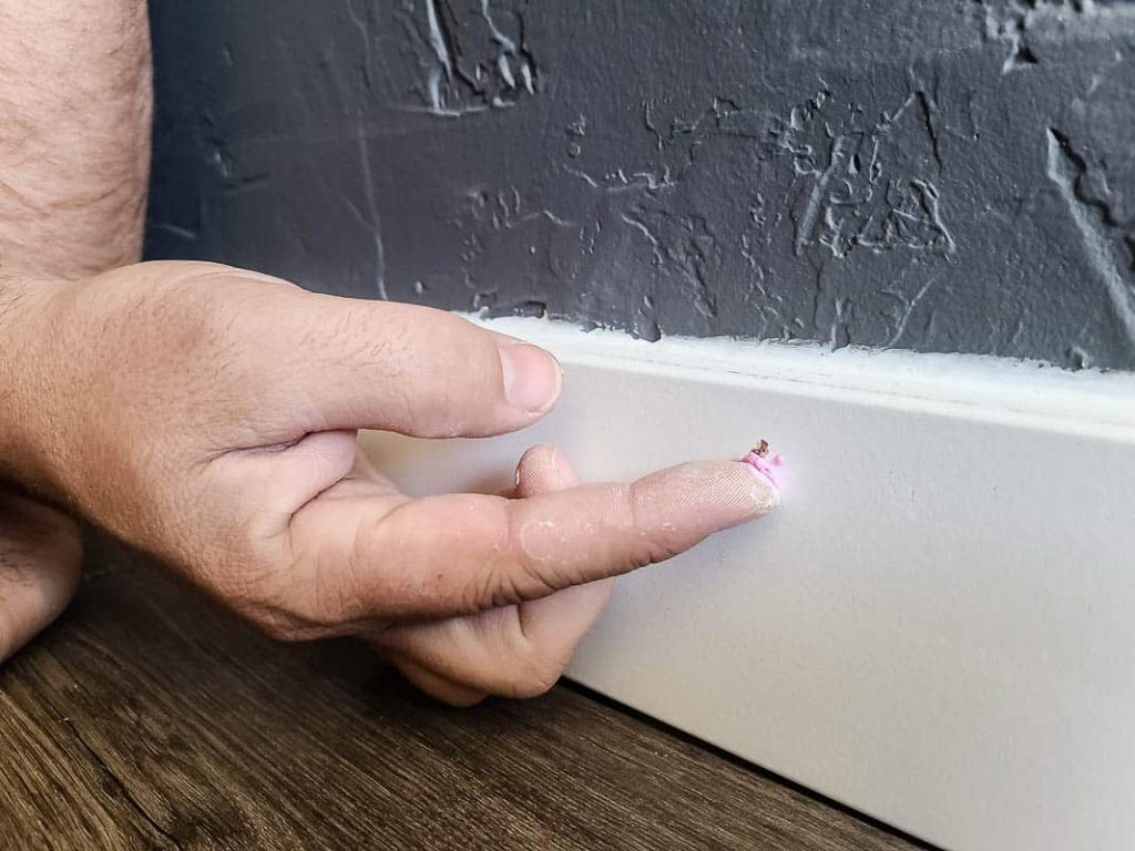 Hand of a man patching nail holes at the trim with spackle