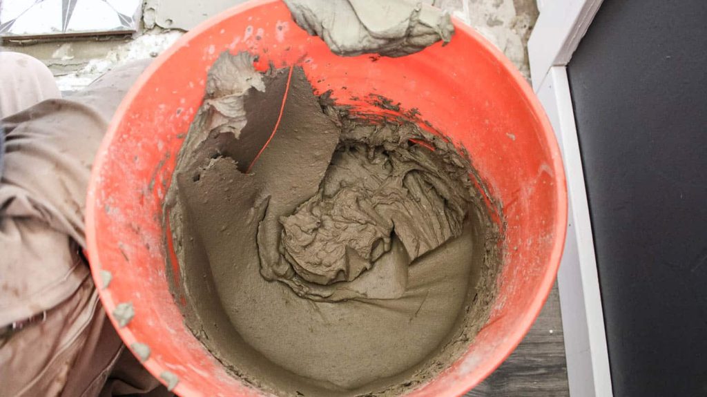 Thinset mortar mixture in the orange bucket with a peanut butter like consistency