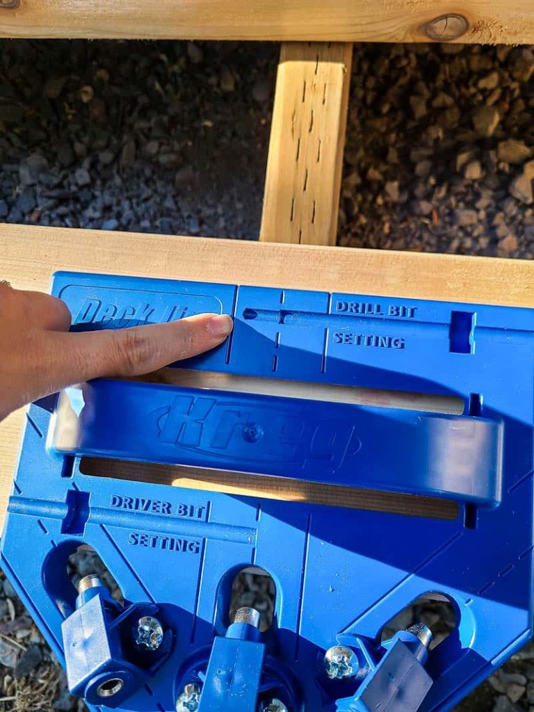 Woman pointing to the deck jig on top of the wood showing how to line up the deck jig to the joists in the deck frame