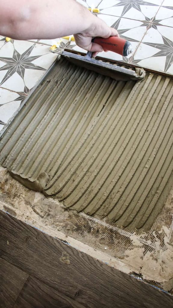 Man applying mortar on cement subfloor and creating grooves with a notched trowel before laying down large format tile into place