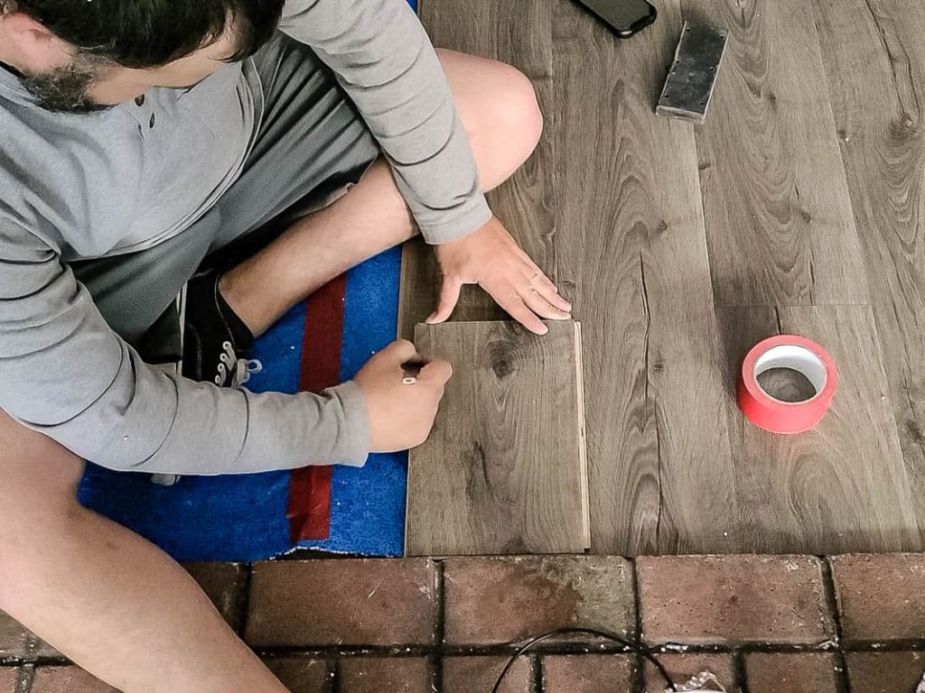 Man sitting on the floor marking a part of the laminate piece and red tape on the laminate floor