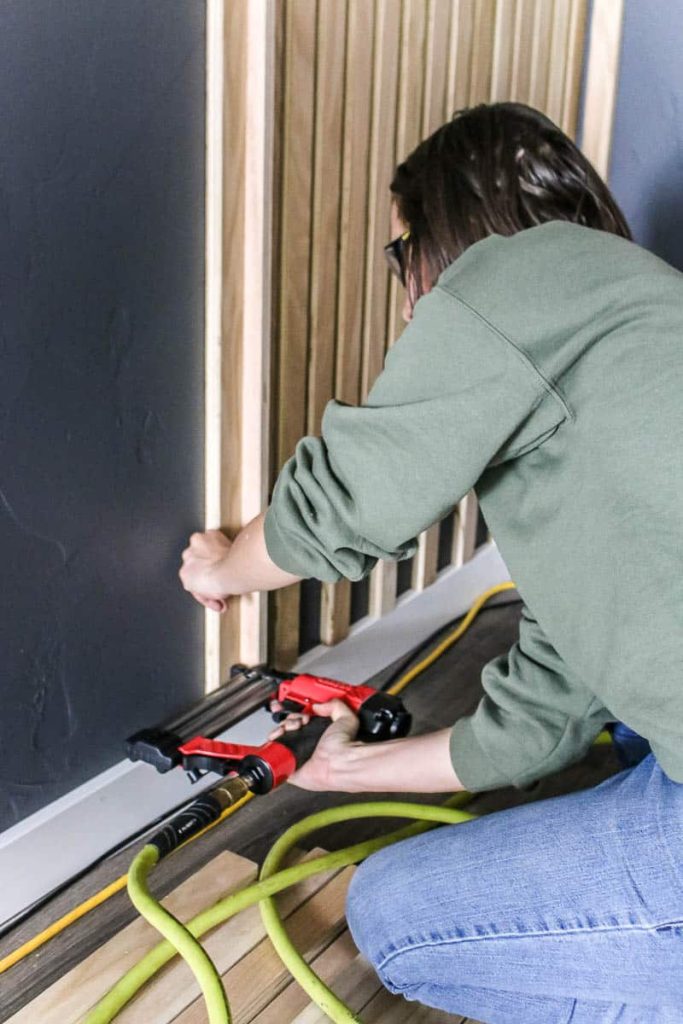 Woman holding a brad nailer attaching the wood slats on the wall