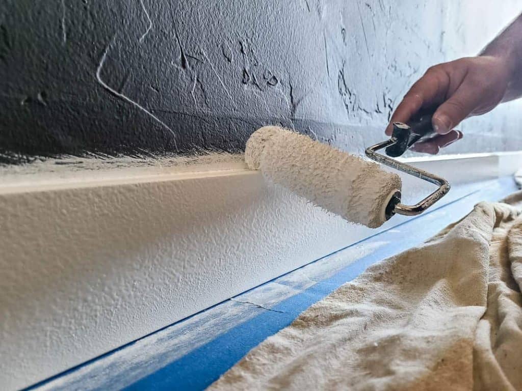 Using a paint roller to paint the top of a baseboard.