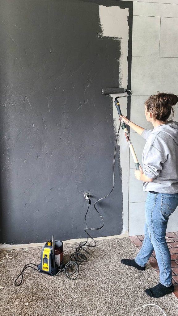 Woman holding electric roller painting the entire wall with gray paint