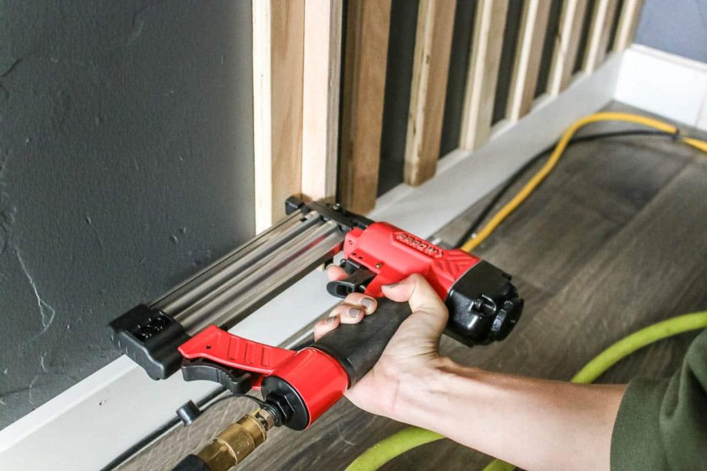 Woman nailing the wood slat in the wall using brad nailer