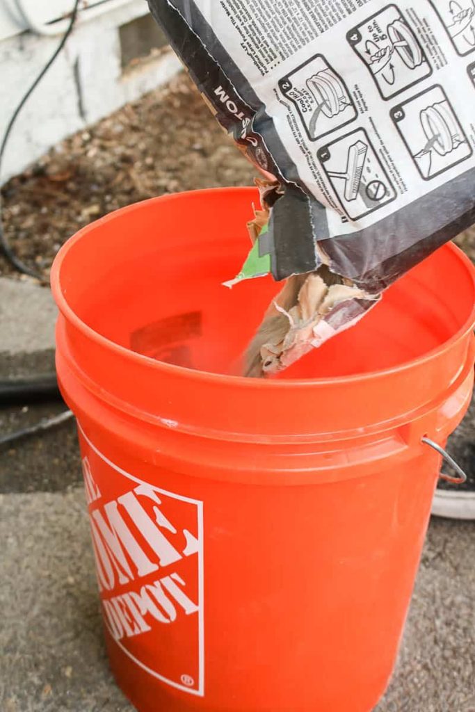bag of thinset mortar being poured into orange bucket before being mixed
