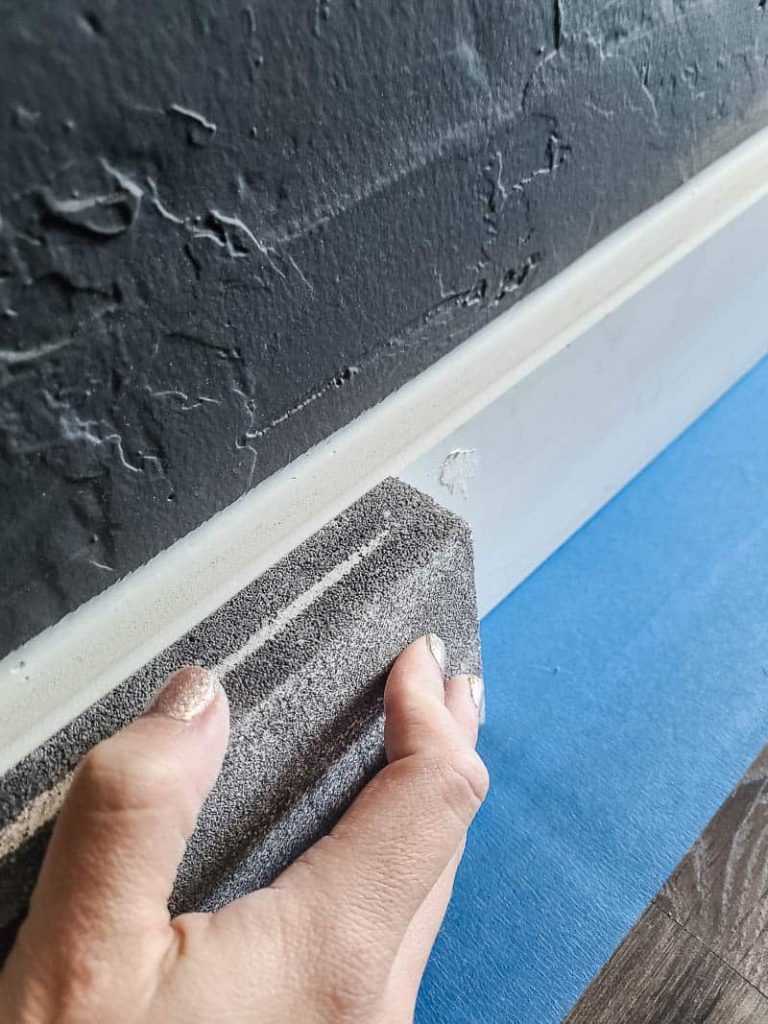 Close up of woman sanding the baseboard with sanding sponge before painting