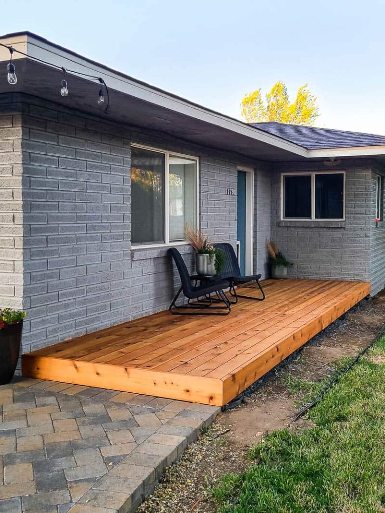 Full view of backyard with wood deck, chairs, center table, plants, windows and back door