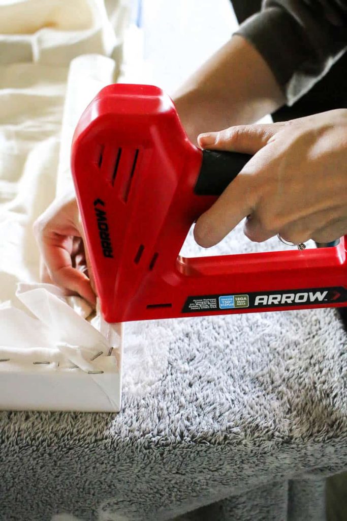 Woman stapling the fabric tapestry on to the wood frame using electrical stapler