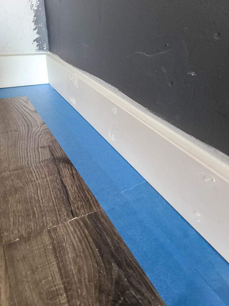 Blue painters tape on the floor next to the baseboard to keep paint from getting on the floor