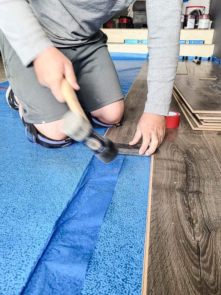 Man holding hammer attaching the laminate floors tightly together on top of the underlayment