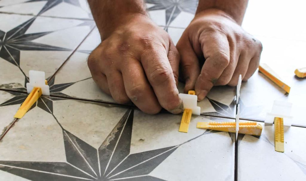The white part of the spacer goes at the end of the tile and tucks underneath the tile. Then the yellow wedge slides into the hole of the spacer and clicks into place while pushing the tiles down to ensure they are level with each other.