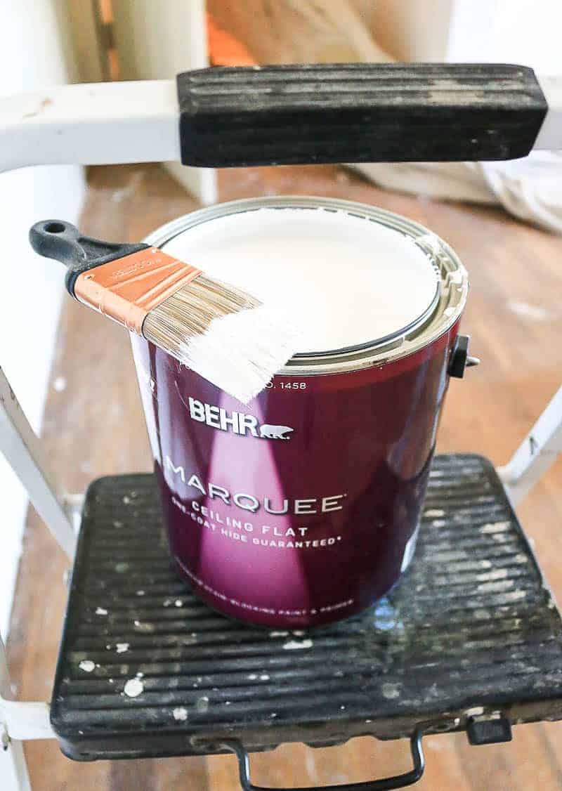 can of white flat ceiling paint sitting on step stool with a paint brush laying on top of it
