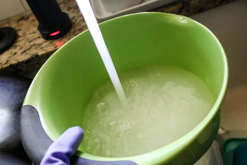 how to clean walls before painting, water pouring from sink added to the TSP powder filling the green container