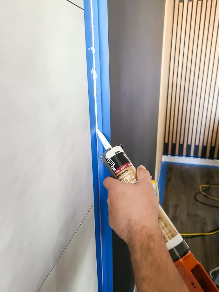 Then, we applied a small bead of 100% silicone caulk in white where the fireplace panels and the wood trim met and where the panels and the ceiling came together. This gives it a nice professional-looking finish to this fireplace makeover.