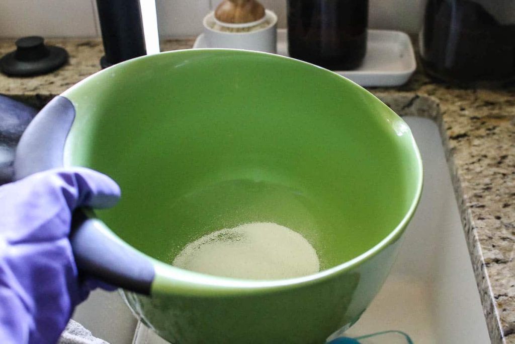 how to clean walls before painting a woman wearing gloves holding a green container with TSP poweder