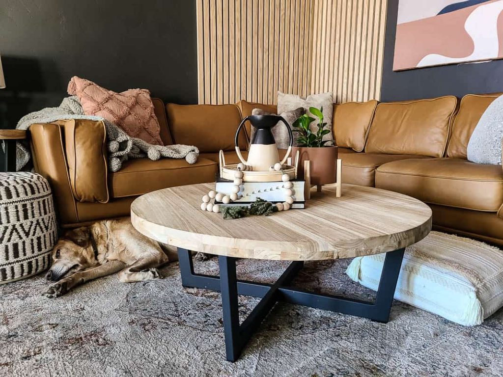 Closeup of seating area with Article Timber sectional in light brown, coffee table styled with books, tray and plant, wood slat accent wall and a lab sleeping between the sectional and Article teak wood coffee table.