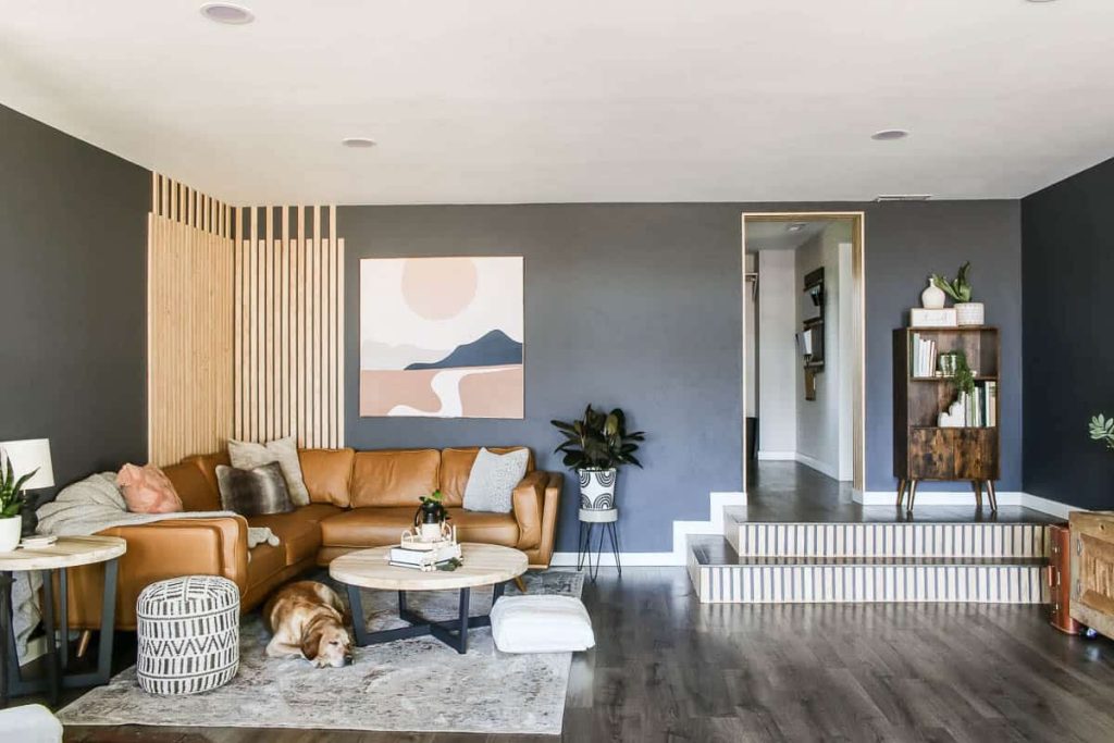 After photo of modern boho living room with light brown cognac Article Timber leather sectional in corner with wood slat wall, round coffee table, tapestry wall art, a Lab laying asleep on large area rug in front of sectional and finished step.