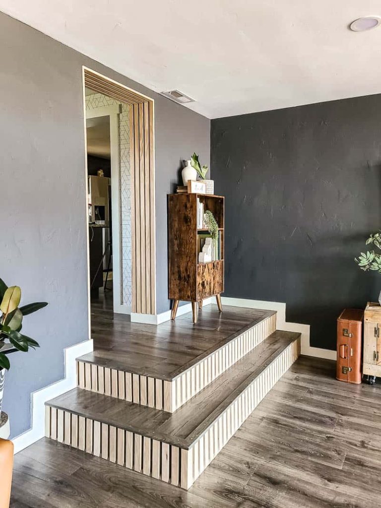 Image of step makeover with wood slats on risers and new laminate flooring with mid century modern bookcase. The before and afters of this modern boho living room renovation.