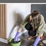 Woman wearing gloves dipping a cloth on a green bowl with text overlay that says how to clean walls before painting